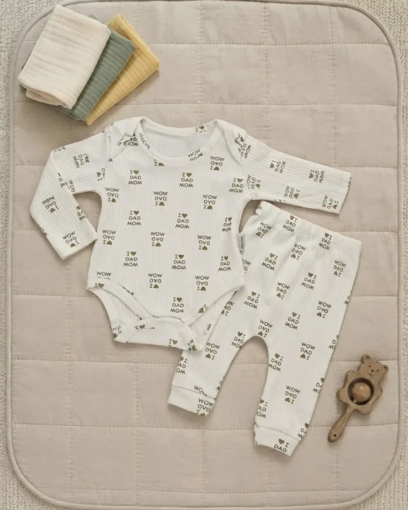 Beyaz renkli, Mom Dad yazı ve kalp baskılı uzun kollu çıtçıtlı body ve manşetli pantolondan oluşan 2 parça unisex bebek takımı – stilist ürün parçaları kompozisyonu
