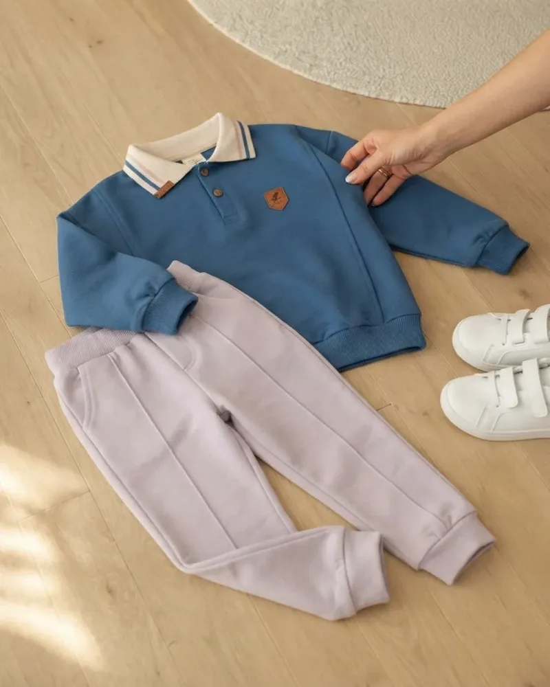 Erkek çocuk mavi polo yakalı uzun kollu üst ve açık renk pantolon takım giymiş model – stilist ürün parçaları kompozisyonu